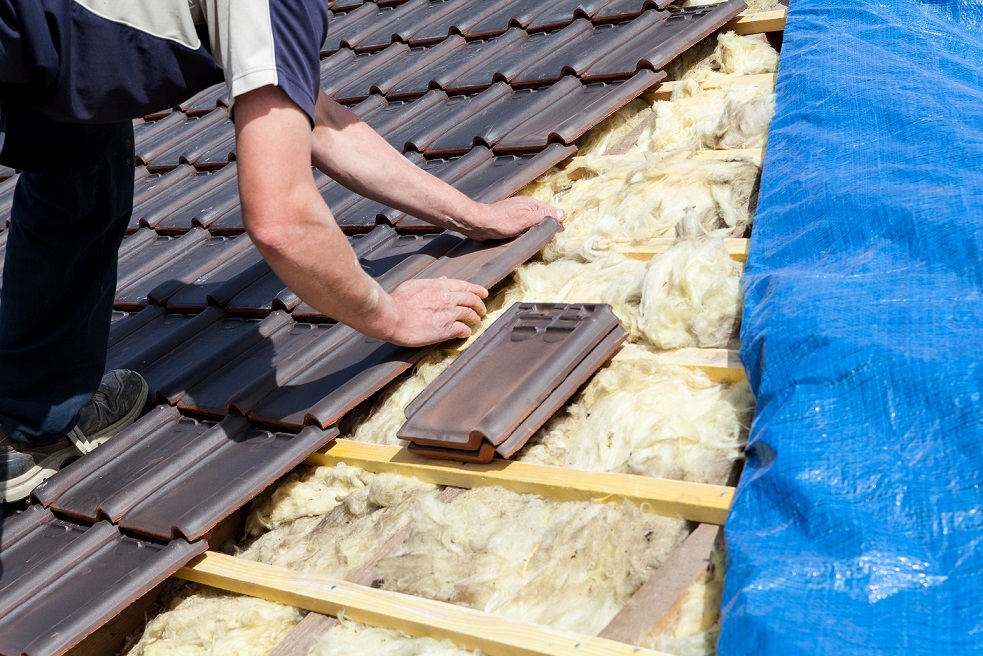 mężczyzna montuje grafitową, ceramiczną dachówkę, klamrując ją do połaci dachu